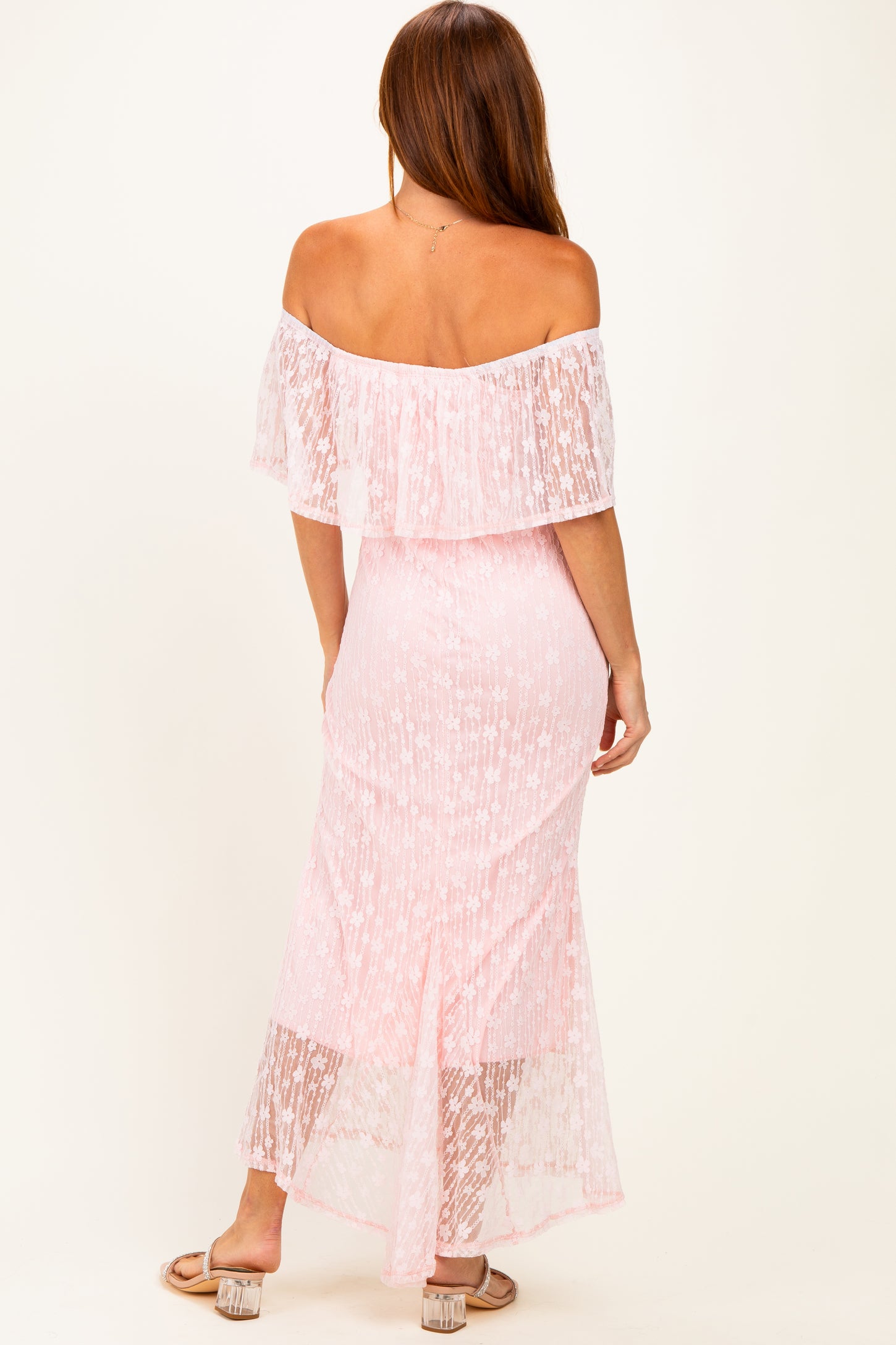 woman wearing a light pink off-the-shoulder maxi dress with a ruffled overlay and sheer lace details