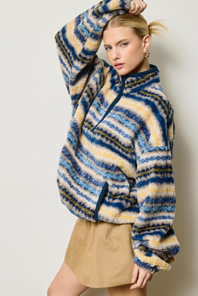woman wearing a multicolored faux fur pullover with a half zip and a striped pattern, styled with a tan skirt