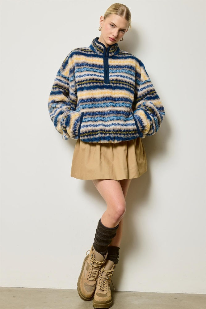 woman wearing a blue and cream striped fleece pullover with a half zip, paired with a tan skirt and knee-high socks
