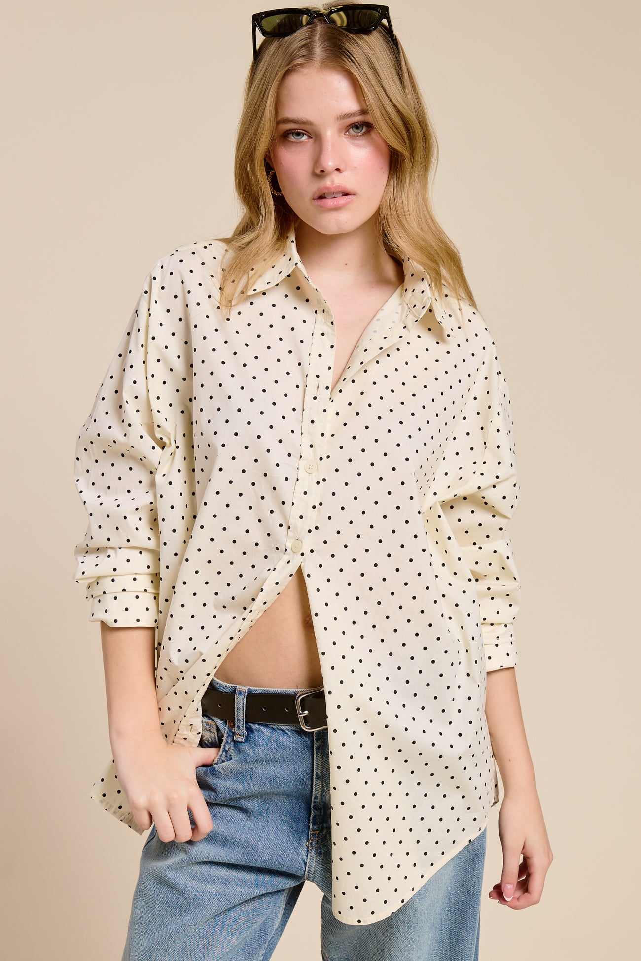 woman wearing a cream button-up shirt with black polka dots and distressed jeans, styled with sunglasses in her hair
