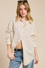 woman wearing a cream button-up shirt with black polka dots and distressed jeans, styled with sunglasses in her hair