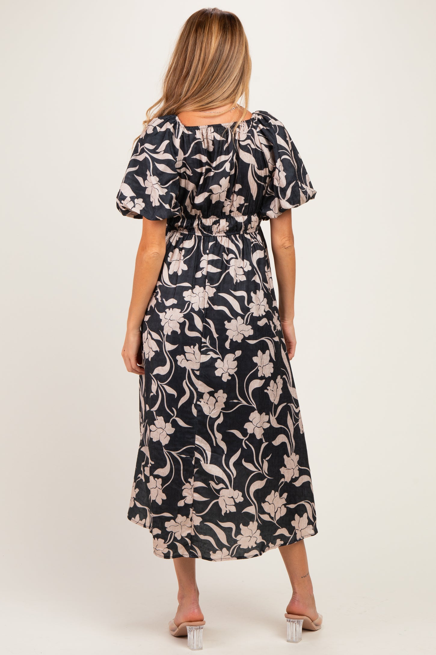woman wearing a floral patterned black maternity dress with puff sleeves and an elastic waist, seen from the back