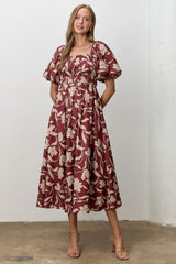 woman wearing a burgundy floral midi dress with puff sleeves and a fitted smocked bodice