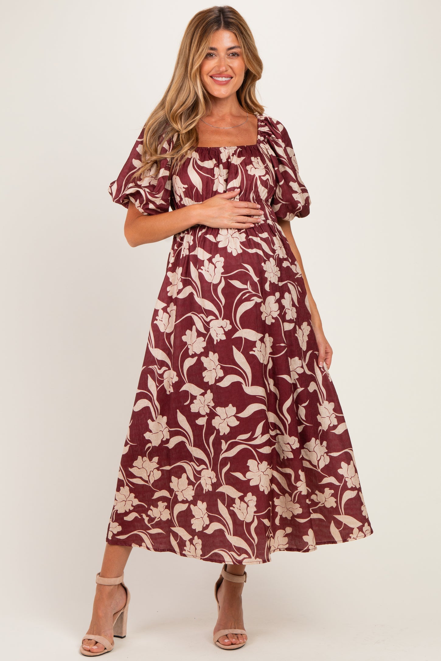 woman wearing a burgundy floral print maternity dress with puff sleeves and holding her baby bump