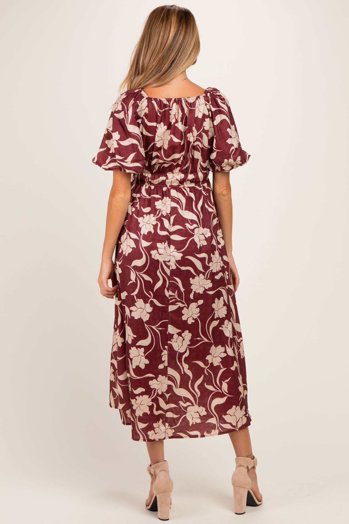 woman wearing a burgundy floral maternity dress with puff sleeves and an elastic waist, seen from behind