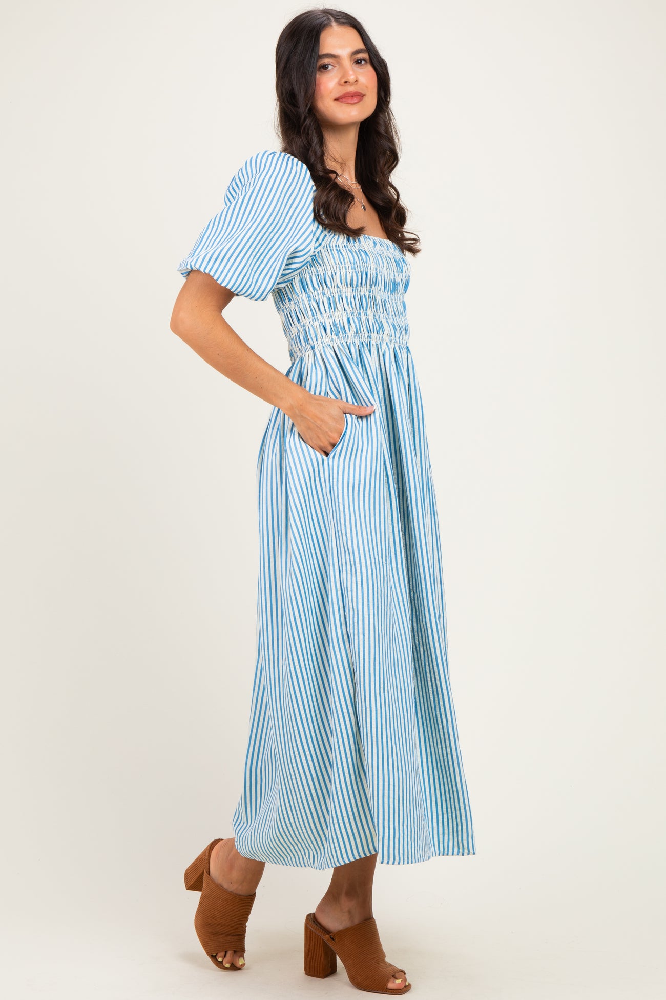 woman wearing a blue and white striped maxi dress with puffed sleeves and pockets, standing in profile