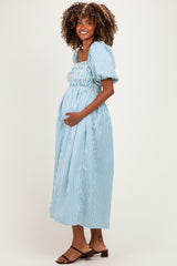 woman wearing a light blue striped maternity dress with puff sleeves and smocked bodice, holding her baby bump