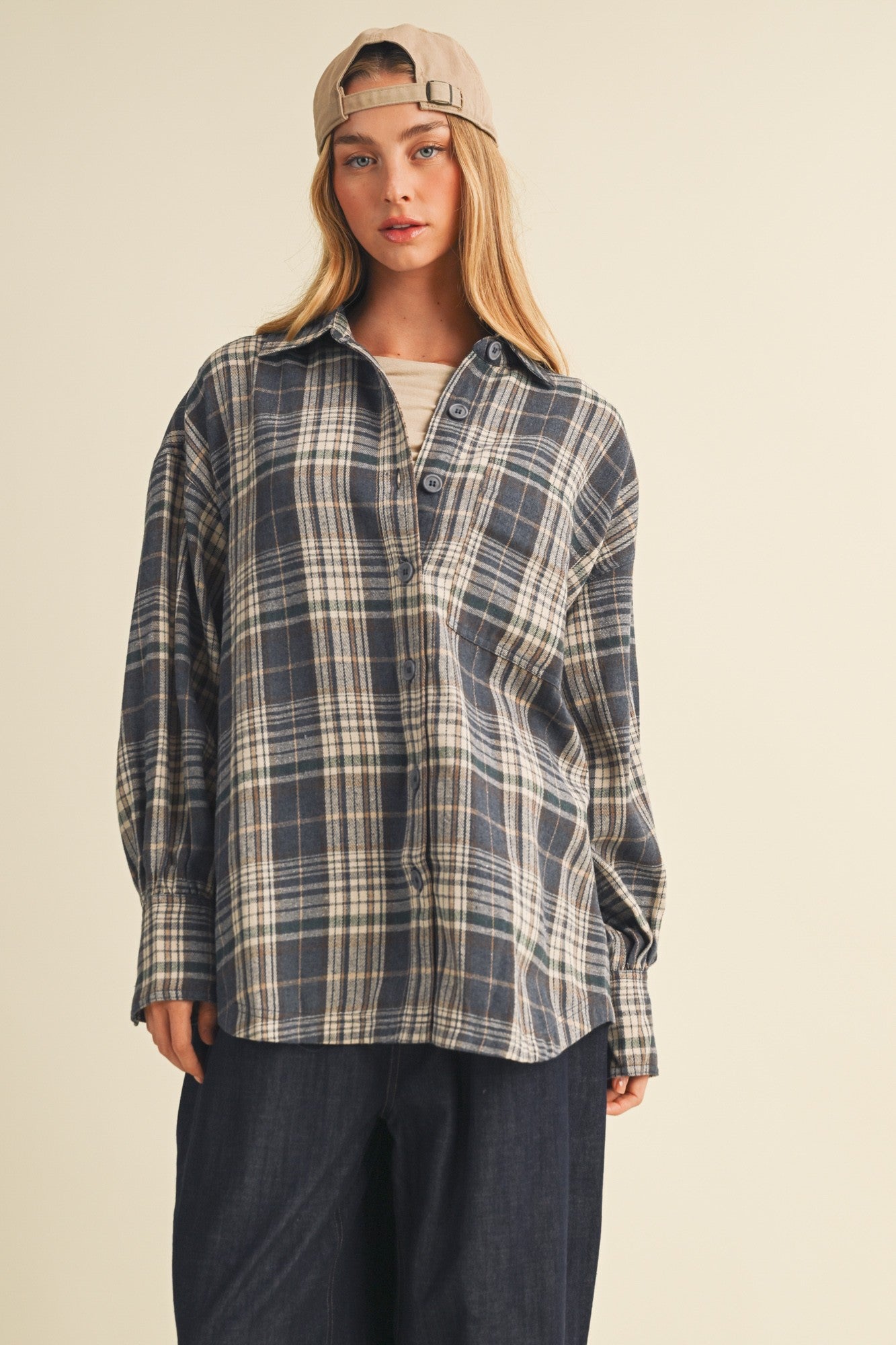 woman wearing a navy and cream plaid button-up shirt with a relaxed fit and a beige baseball cap