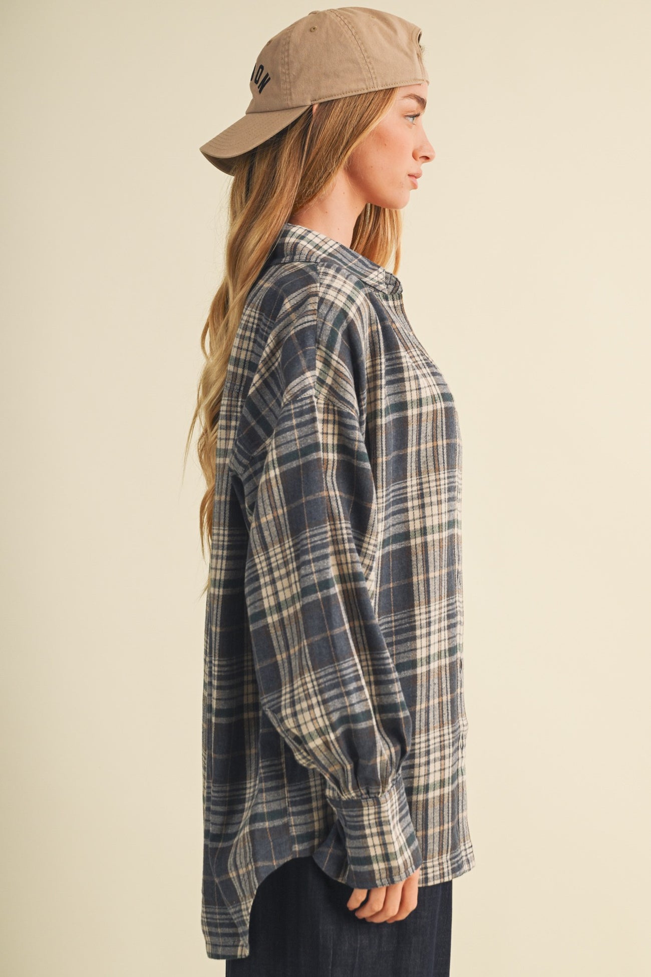 woman wearing a navy and beige plaid oversized shirt with long sleeves and a beige baseball cap