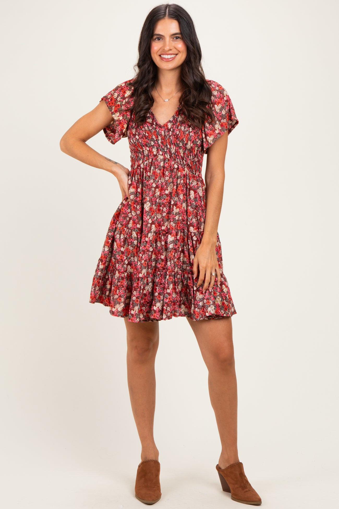woman wearing a red floral short sleeve dress with a smocked bodice and a flared skirt, standing with one hand on her hip