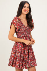 woman wearing a red floral short dress with puff sleeves and a smocked bodice, smiling against a light background