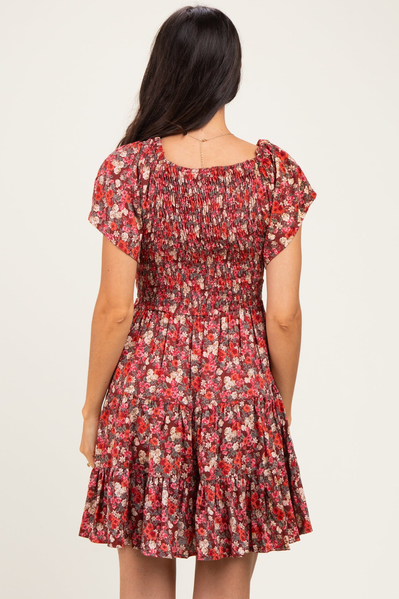 woman wearing a red floral short dress with smocked bodice and flared skirt, shown from the back