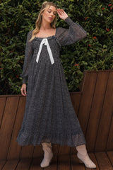 woman wearing a black and white patterned maternity dress with long sleeves and a bow detail, posing outdoors