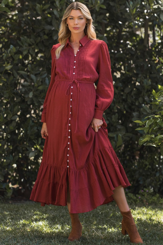 woman wearing a burgundy maternity dress with button details, a drawstring waist, and a ruffled hem, showcasing her baby bump