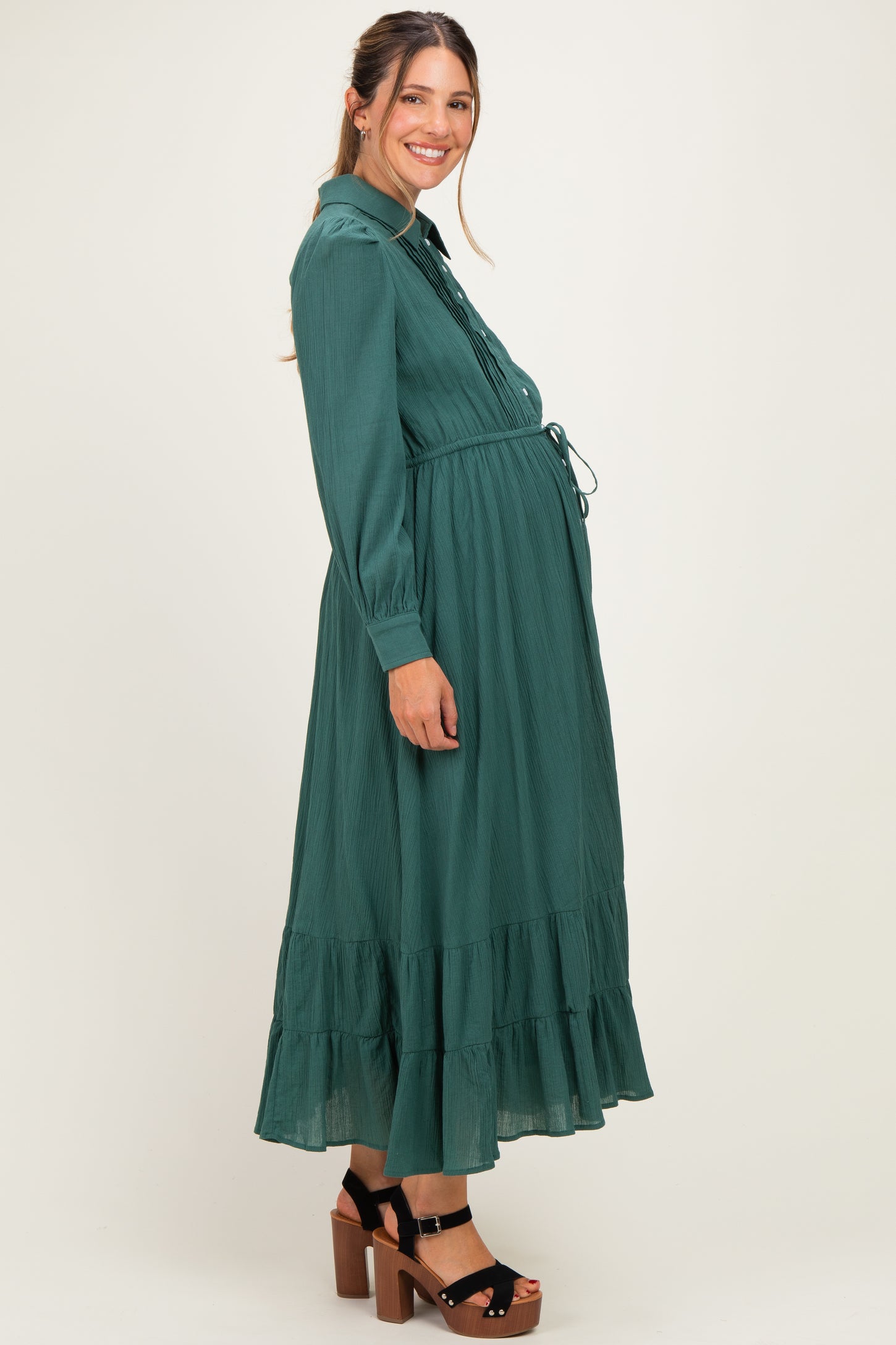 woman wearing a dark green long sleeve maternity dress with a tiered skirt and visible baby bump