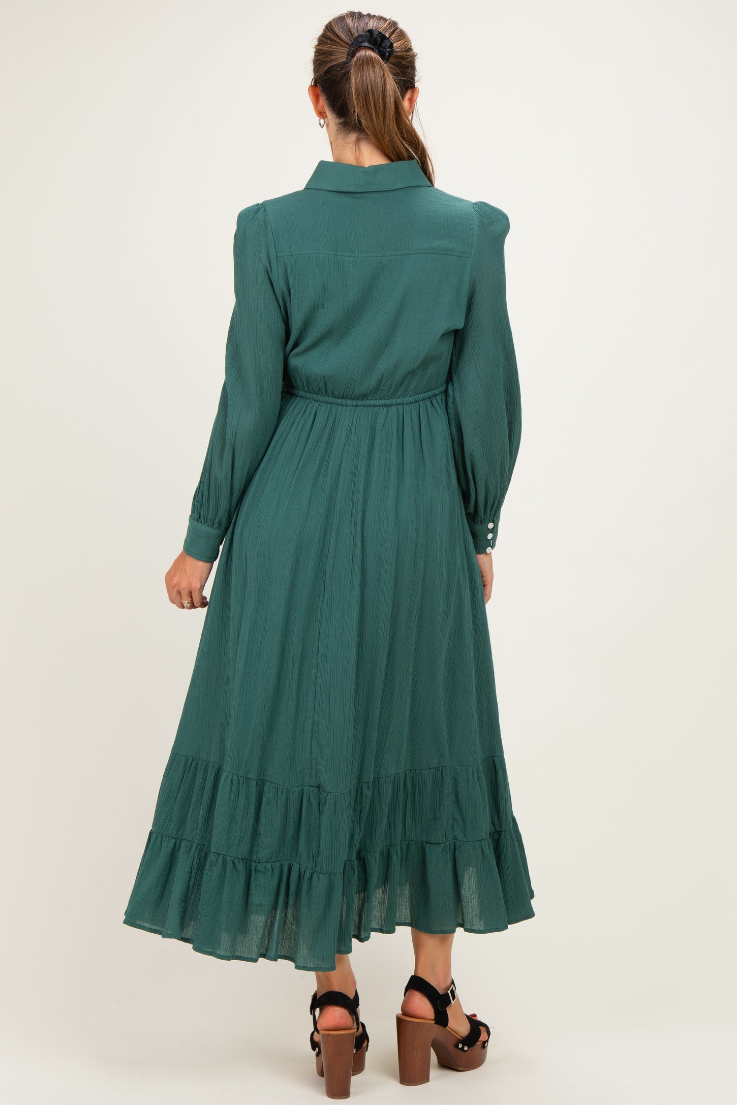woman wearing a dark green maternity dress with a tiered skirt and long sleeves, showing the back view