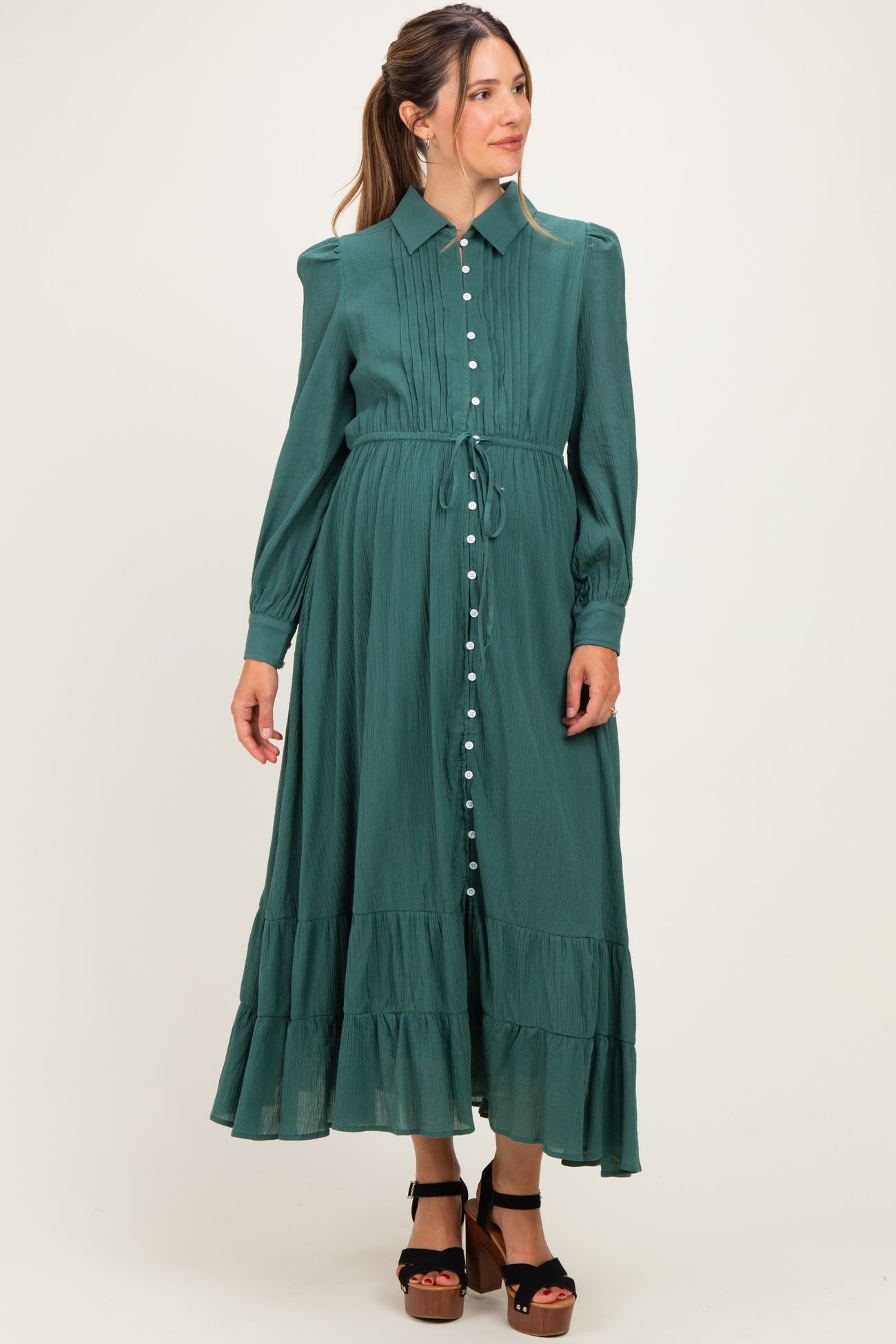 woman wearing a green maternity dress with a button-up front and ruffled hem, styled with a tie waist and long sleeves