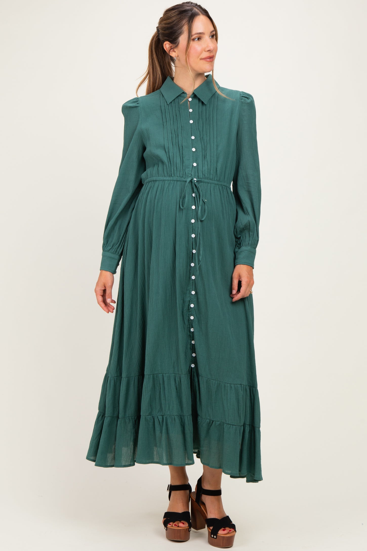 woman wearing a green maternity dress with a button-up front and ruffled hem, styled with a tie waist and long sleeves
