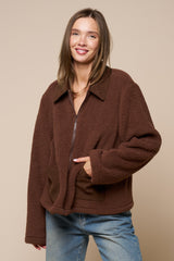 woman wearing a brown zip-up fleece jacket with large pockets and a collared neckline, styled with blue jeans