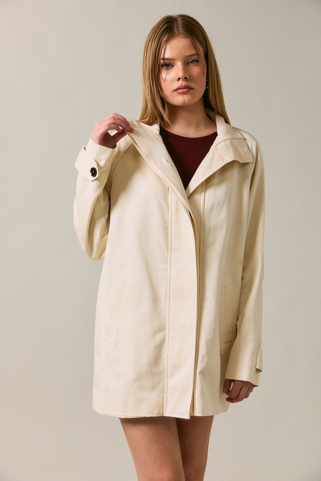 woman wearing a cream-colored casual jacket with a collar and front pockets, standing against a neutral background