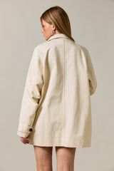 woman wearing an oversized cream-colored jacket with button details, shown from the back