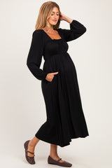 woman wearing a black long sleeve maternity dress with a square neckline and pockets, showcasing her baby bump