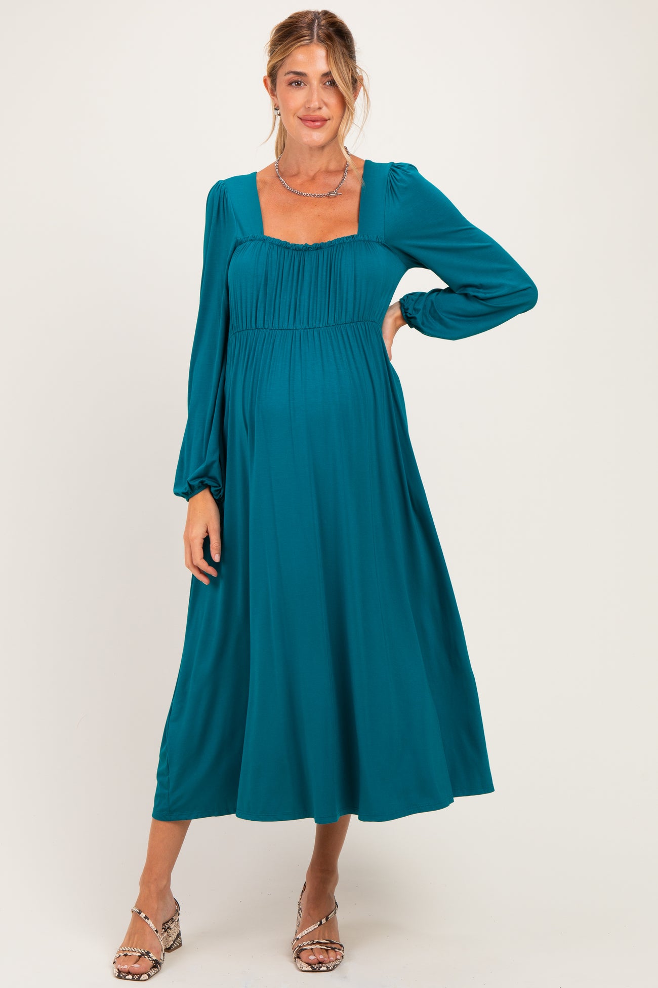 woman wearing a teal maternity dress with a square neckline and long sleeves, showcasing a baby bump