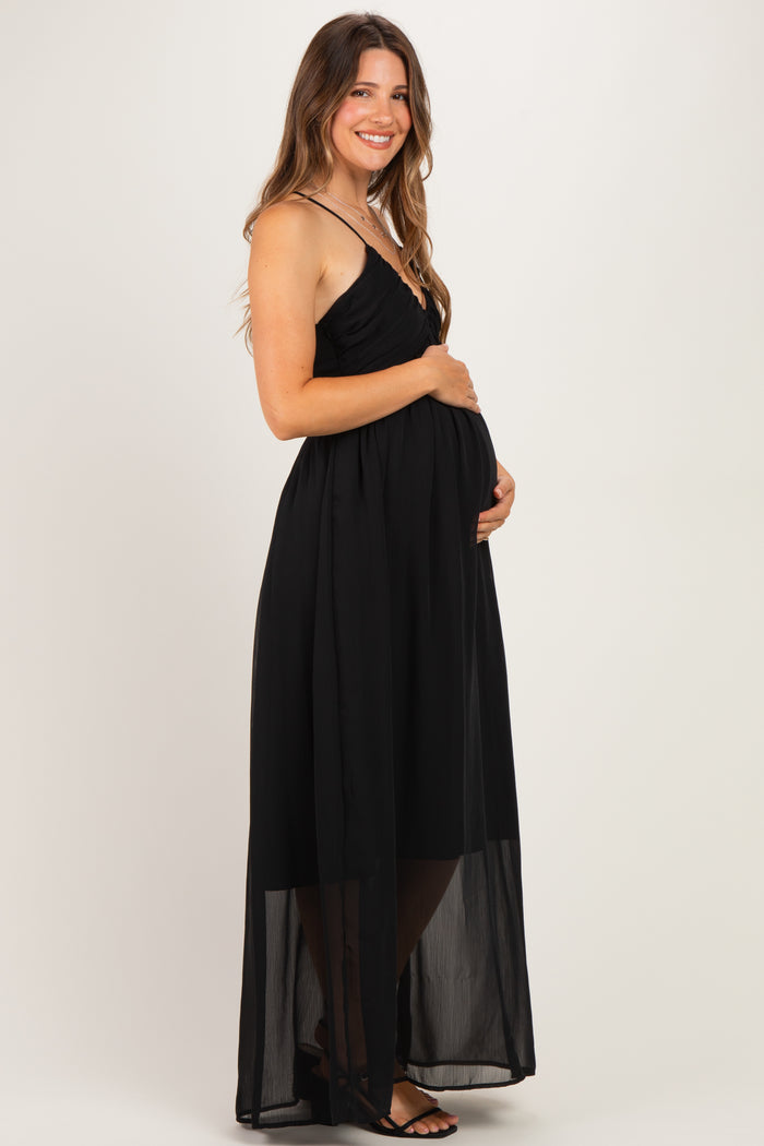 woman wearing a black maternity maxi dress with a sheer overlay and holding her baby bump