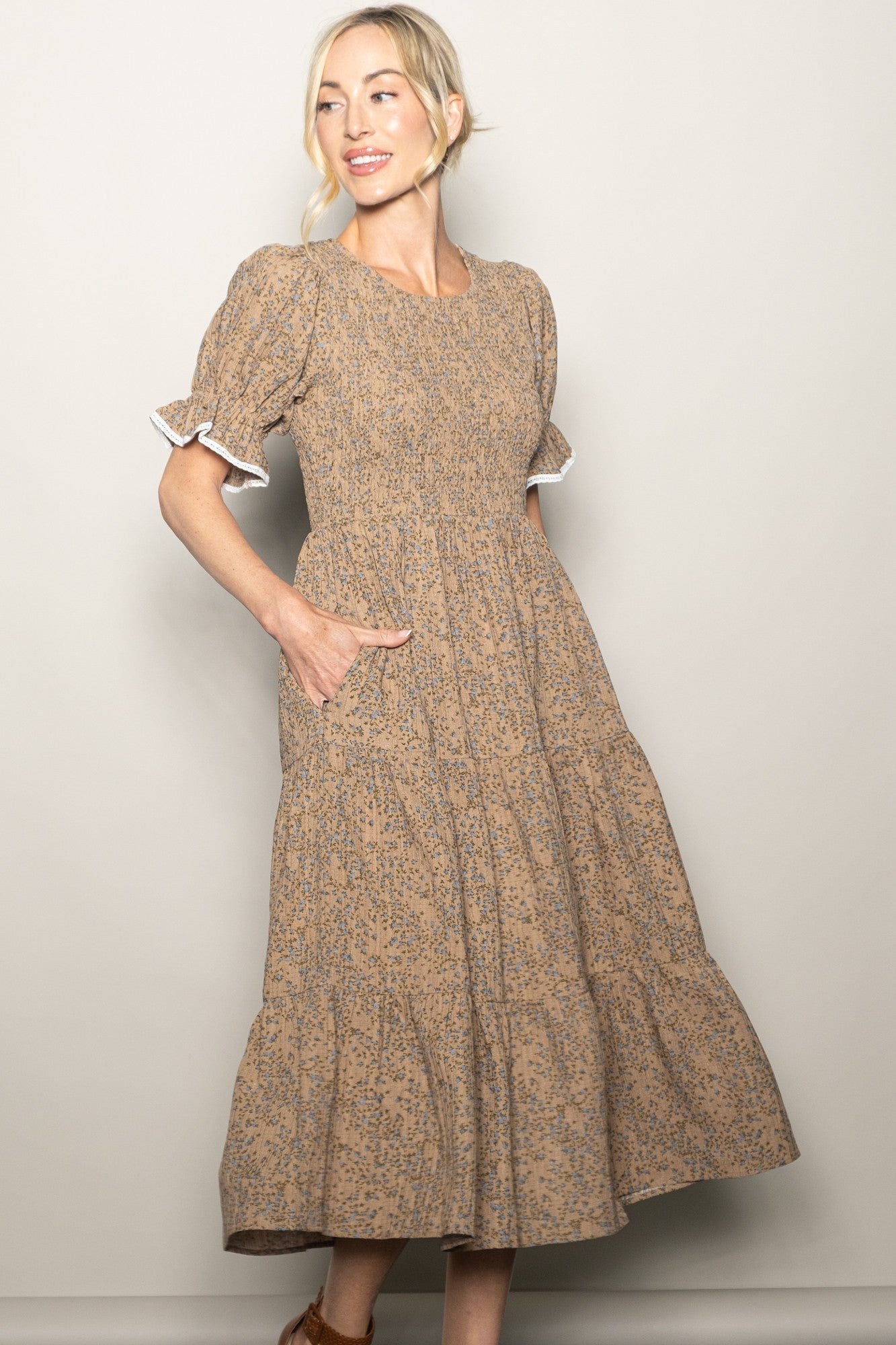 woman wearing a brown floral midi dress with puff sleeves and pockets, standing against a neutral background