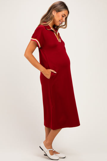woman wearing a burgundy short sleeve maternity dress with pockets and a collar, showing her baby bump