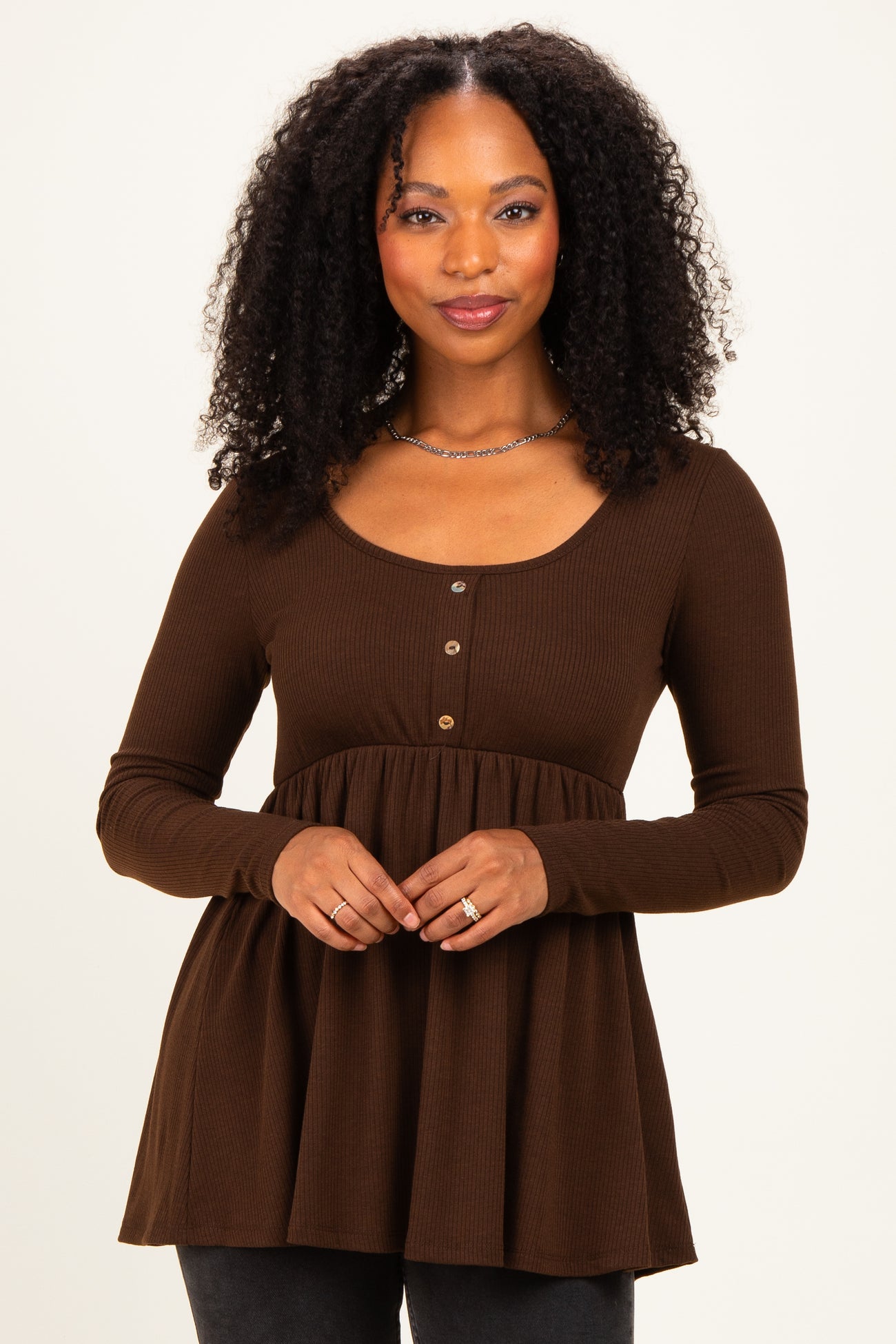 woman wearing a brown long sleeve henley tunic with a flared peplum and button details