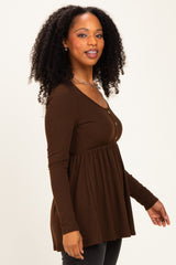 woman wearing a brown long sleeve top with button details and a flared hem, styled with black jeans