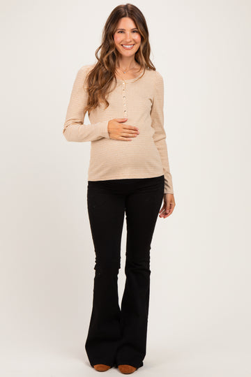 woman wearing a tan striped maternity top with buttons, holding her baby bump and paired with black flared pants