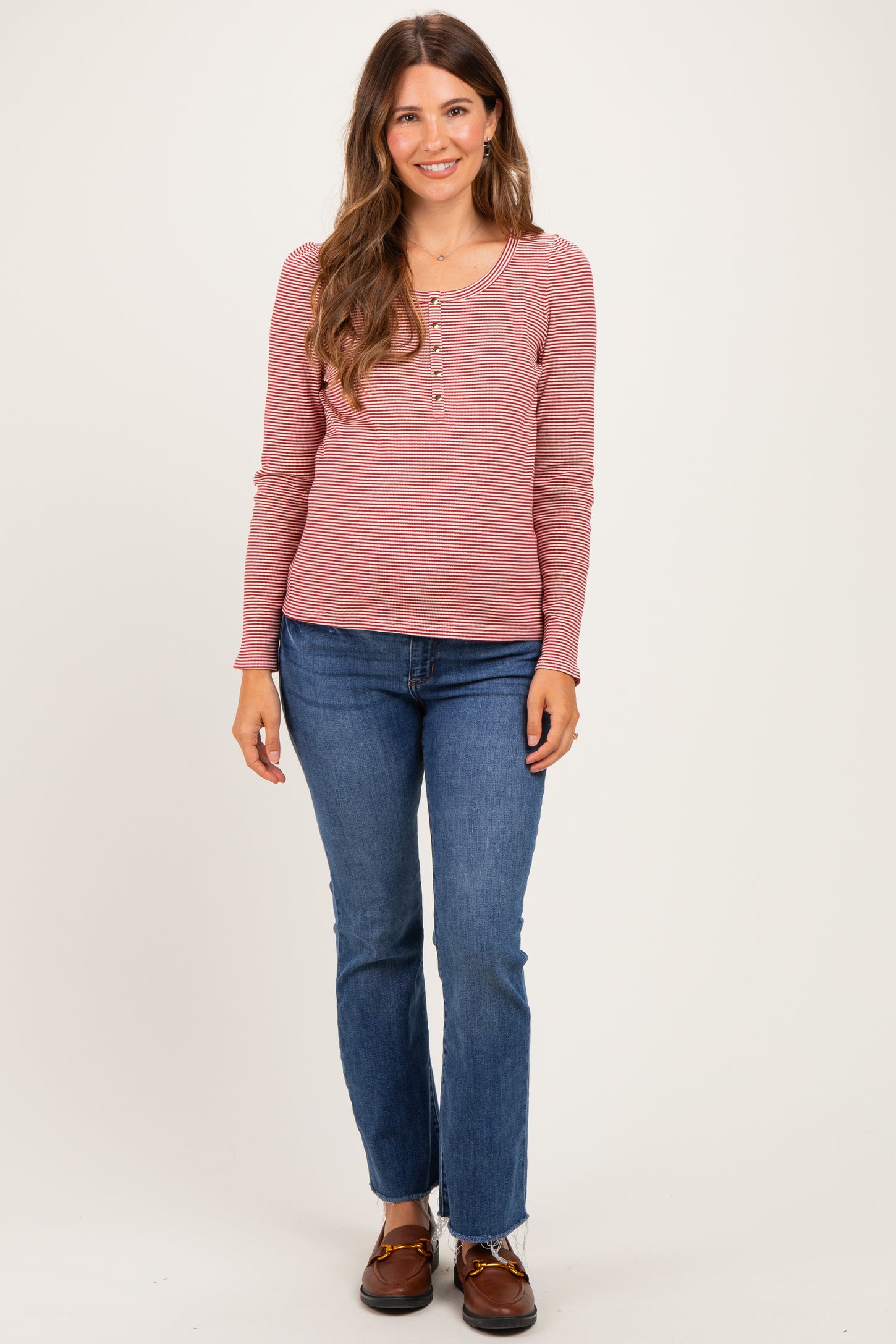 woman wearing a pink and white striped long sleeve maternity top with buttons and denim jeans, showing a baby bump