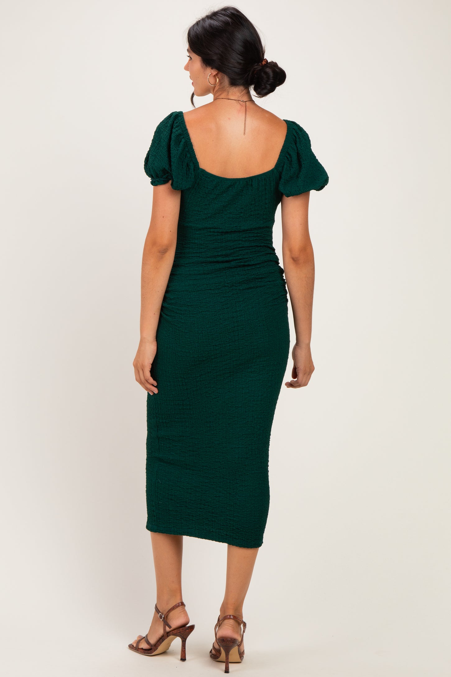 woman wearing a green fitted midi dress with puff sleeves and a ruched design, viewed from the back