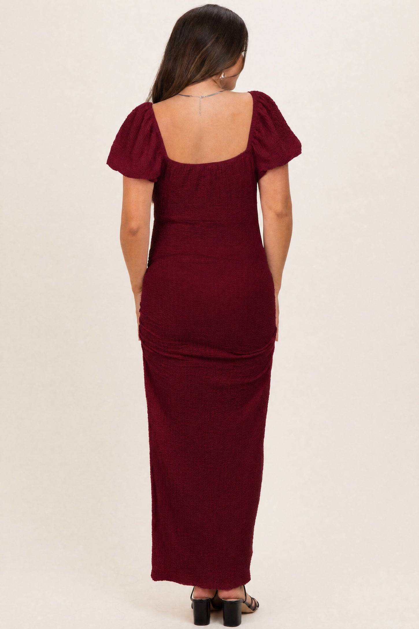 woman wearing a burgundy maternity maxi dress with puff sleeves, showing a smooth back profile