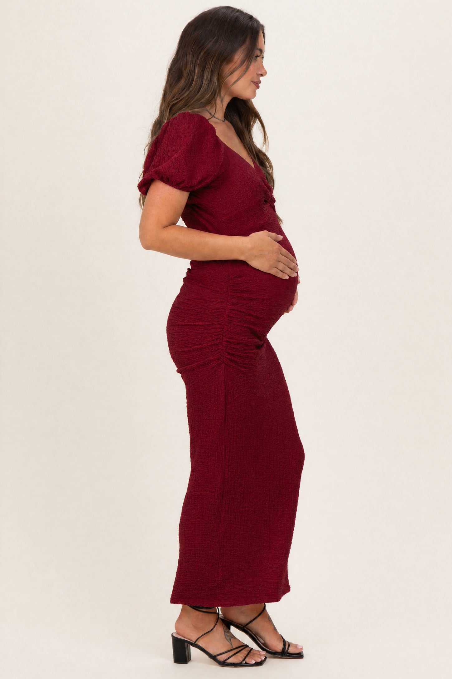 woman wearing a burgundy maternity dress with puff sleeves and side ruching, holding her baby bump