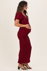 woman wearing a burgundy maternity dress with puff sleeves and side ruching, holding her baby bump