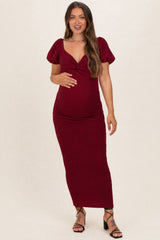 woman wearing a burgundy maternity maxi dress with puff sleeves and gathering at the waist, showing her baby bump
