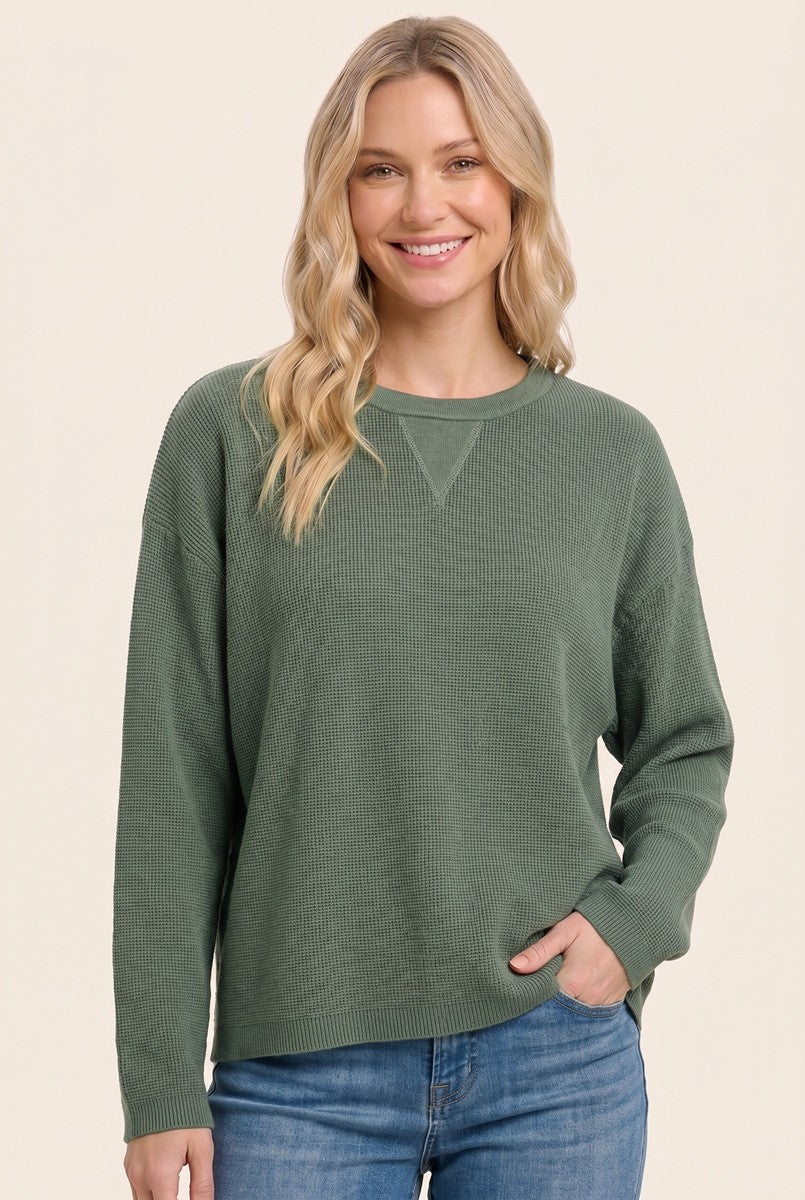 woman wearing a green waffle knit long sleeve top paired with blue jeans, smiling at the camera