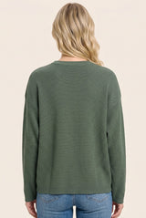 woman wearing a green ribbed long sleeve sweater, viewed from the back, paired with light blue jeans