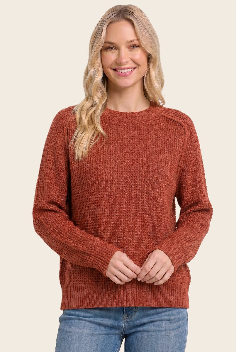 woman wearing a rust colored textured knit sweater with long sleeves and a round neckline, smiling at the camera