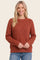 woman wearing a rust colored textured knit sweater with long sleeves and a round neckline, smiling at the camera