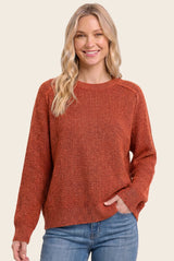 woman wearing a rust-colored knit sweater with a relaxed fit and long sleeves, smiling with hands in pockets