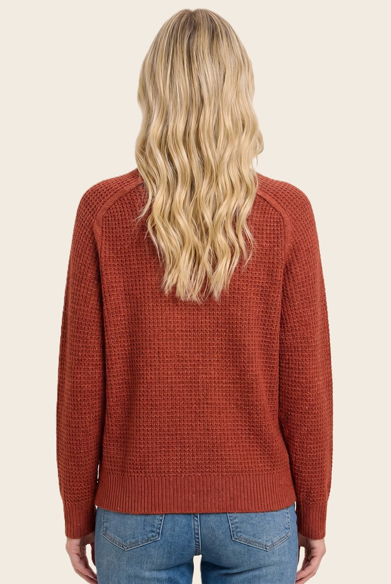 woman wearing a rust-colored textured knit sweater from the back with long wavy hair and light blue jeans