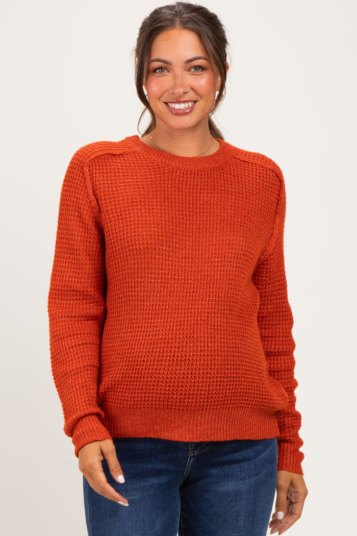 woman wearing a rust orange textured maternity sweater with long sleeves and a relaxed fit, smiling at the camera