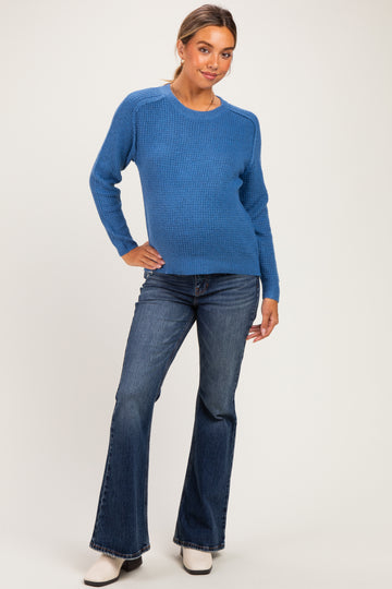 woman wearing a blue knitted maternity sweater paired with flared jeans, showcasing her baby bump