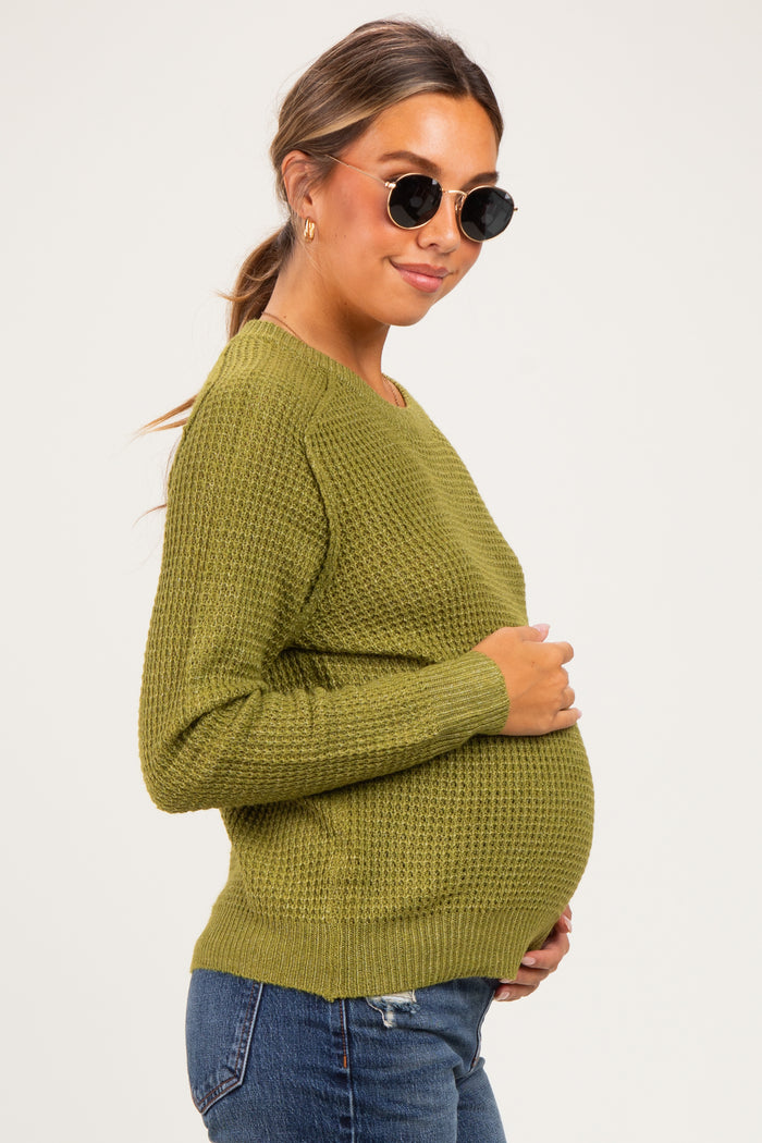 woman wearing an olive green textured maternity sweater and cradling her baby bump in a side view