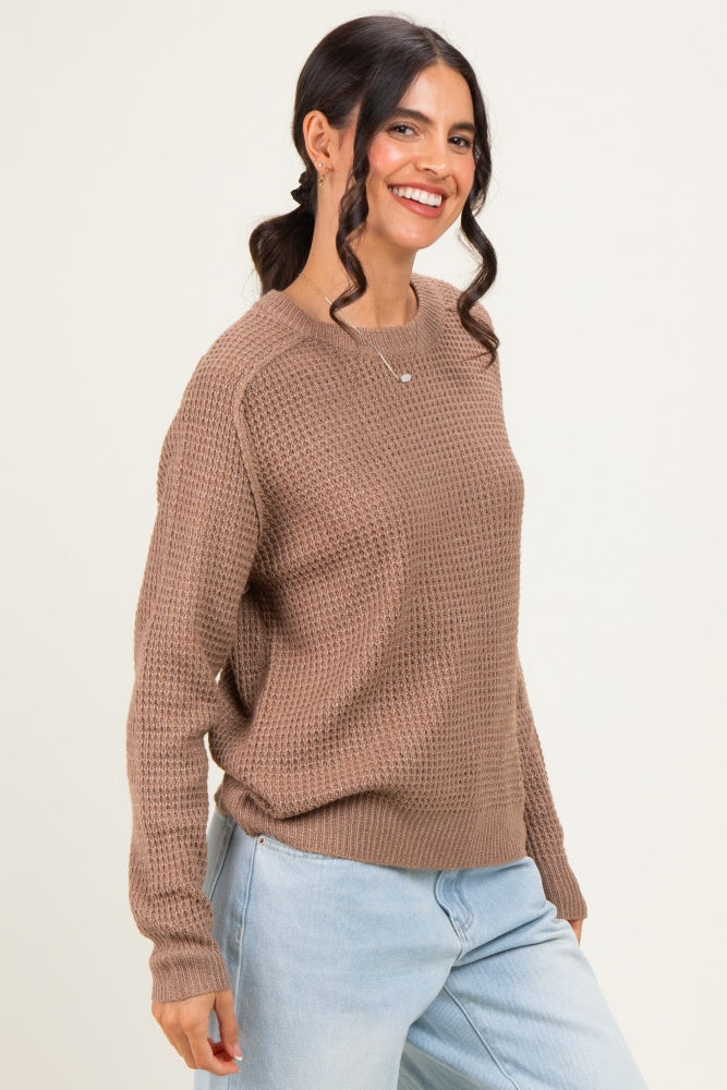 woman wearing a brown textured knit sweater with long sleeves and light blue jeans, smiling at the camera