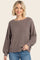 woman wearing a brown oversized knit sweater with a wide neckline and long sleeves, paired with light blue jeans